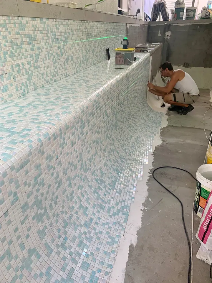 Asher Thomas laying white and aqua mosaic tiles on a pool wall