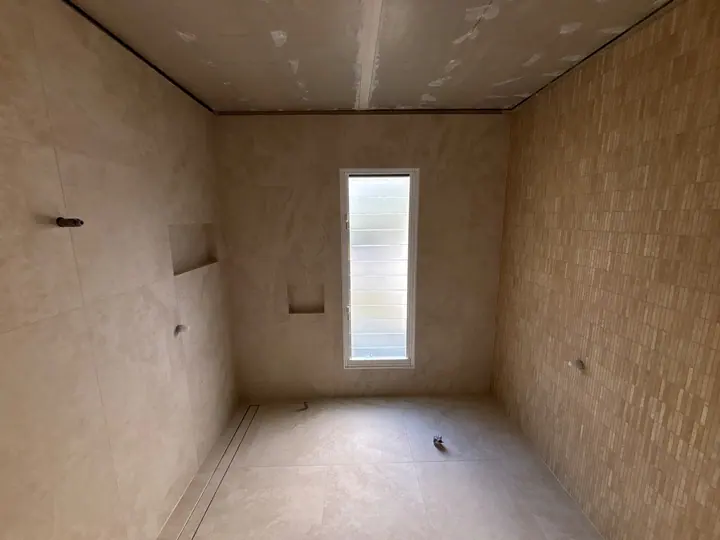 Bathroom walls and floor tiled with a shower niche, ready for fit-out