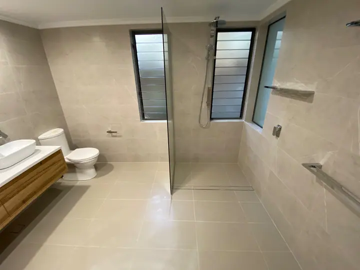 Walk-in shower with a frameless glass screen and beige large-format wall and floor tiles