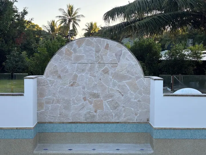 Arched natural stone feature wall above a pool with a blue mosaic waterline