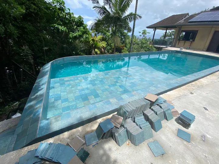 Pool tiling in progress with green-blue tiles stacked on the deck